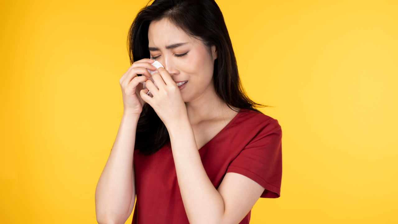 mulher asiática de blusa vermelha chorando em fundo amarelos