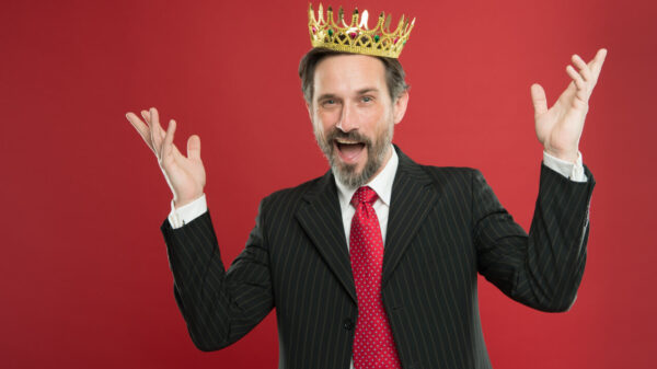 Homem narcisista que se sente superior, com barba, de terno, com uma coroa de ouro na cabeça.