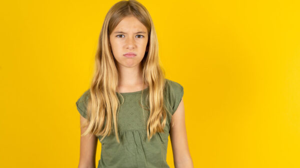 Menina ofendida e insatisfeita, vestindo uma camiseta verde, sobre um fundo amarelo, com uma expressão mal-humorada e descontente com algo.