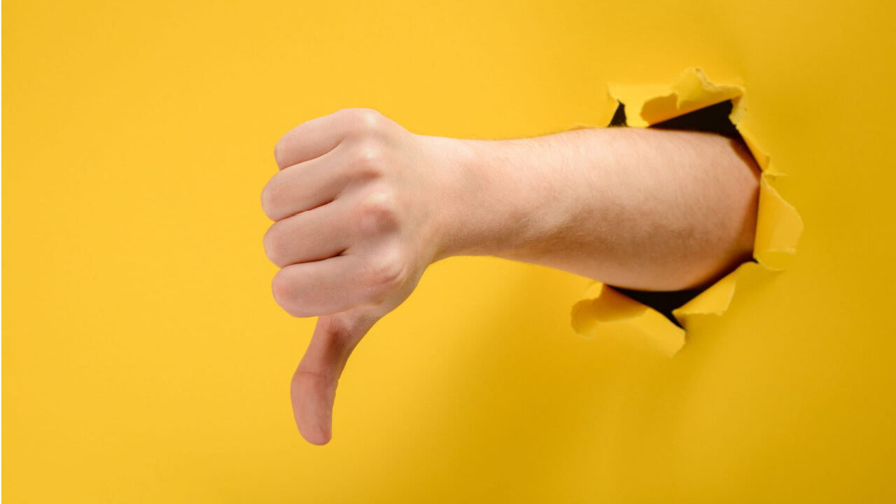Mão com o polegar para baixo através de um buraco rasgado em um fundo de papel amarelo. Gesto de antipatia e desaprovação.