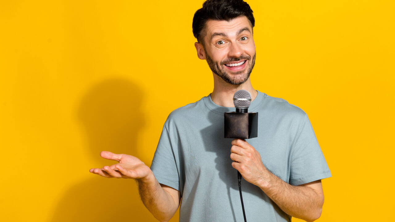 Foto de um homem locutor, positivo, falando em um microfone, dizendo uma notícia, isolado em um fundo de cor amarela.