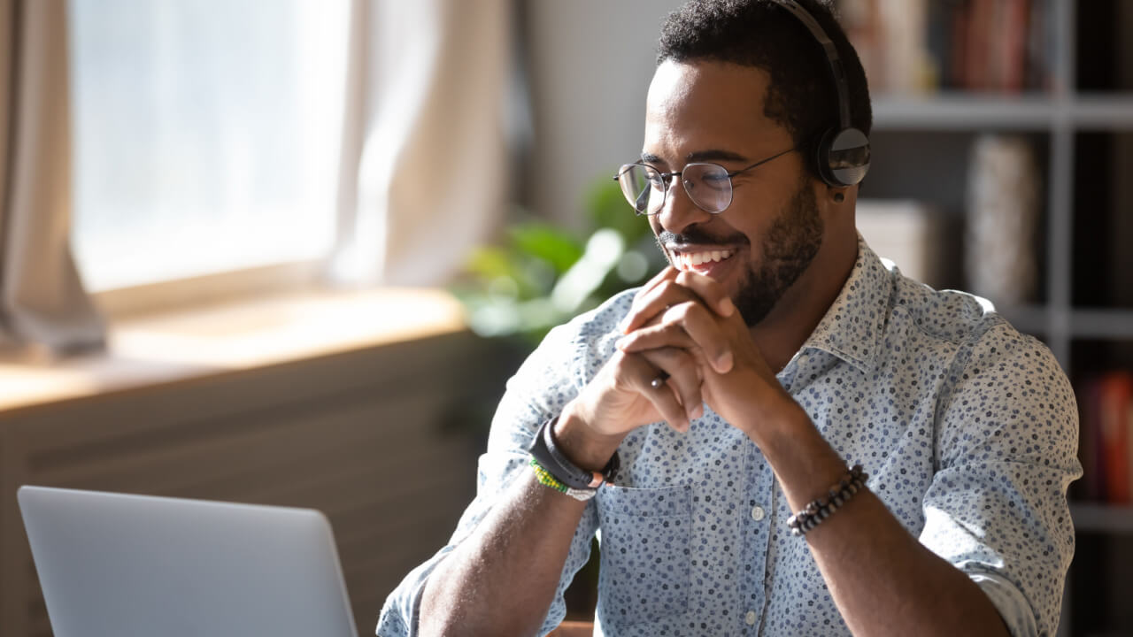 homem negro de camisa social trabalhando em um escritório usando notebook e fone de ouvido