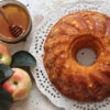 imagem de um bolo de mel visto de cima com um pote de mel e maçãs ao lado