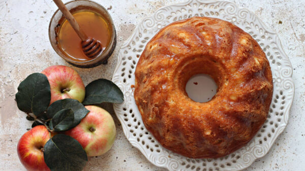 imagem de um bolo de mel visto de cima com um pote de mel e maçãs ao lado