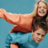 Crianças felizes e alegres. Irmão e irmã em idade escolar brincando junto. O menino leva a menina em suas costas. Fotografia de estúdio em um fundo azul.