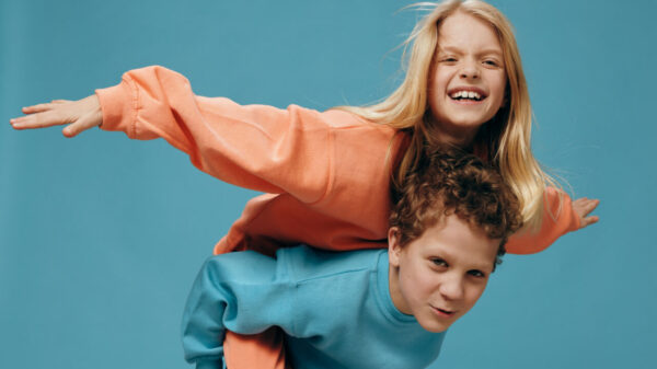 Crianças felizes e alegres. Irmão e irmã em idade escolar brincando junto. O menino leva a menina em suas costas. Fotografia de estúdio em um fundo azul.