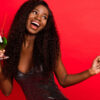 Foto de uma mulher alegre, feliz, sorrindo positivamente, divertindo-se, segurando um drink, isolada sobre um fundo de cor vermelha.