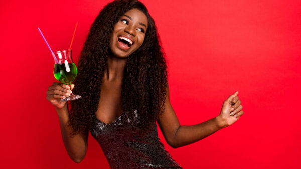 Foto de uma mulher alegre, feliz, sorrindo positivamente, divertindo-se, segurando um drink, isolada sobre um fundo de cor vermelha.