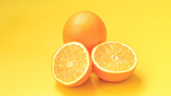duas frutas laranjas e uma está partida ao meio em fundo laranja