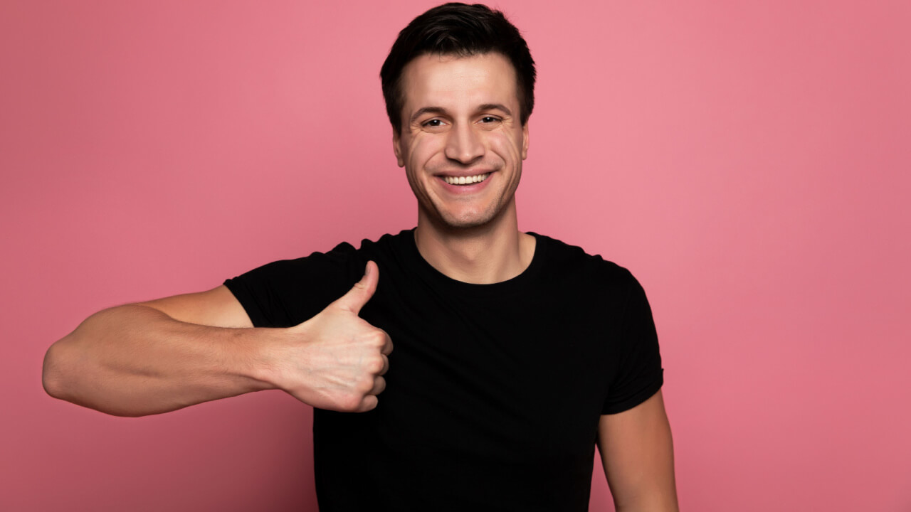 Foto de um homem feliz usando uma camiseta preta, olhando para a câmera com um grande sorriso e com um polegar para cima.