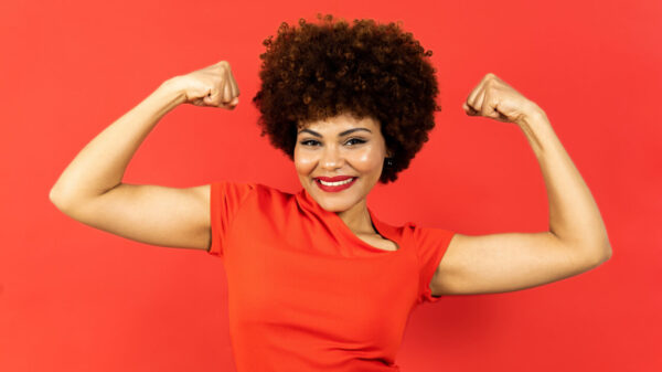 Mulher posando sobre um fundo vermelho, mostrando os dois bíceps, com expressão de incentivo ou motivação.