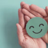 Mãos segurando um rosto de papel verde sorrindo. Conceito de bem-estar.