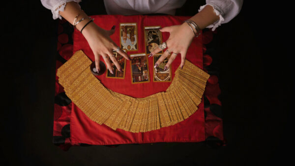 Vista superior de cartas de tarô e das mãos de uma cartomante prevendo o passado e o futuro em um ambiente escuro.