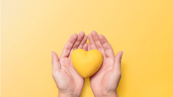 Mãos segurando um coração de resina amarela contra um fundo amarelo correspondente, simbolizando a conscientização sobre a saúde mental e o significado do Setembro Amarelo. Conceito de bem-estar mental e prevenção do suicídio.