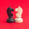 Peças de xadrez de cavalo branco e cavalo preto, tradicionalmente confrontados no jogo de xadrez, reconciliando-se. Imagem em um fundo vermelho isolado.
