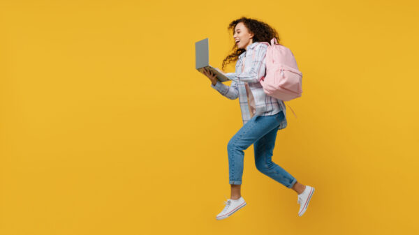 mulher pulando com uma mochila rosa nas costas e notebook na mão em fundo amarelo