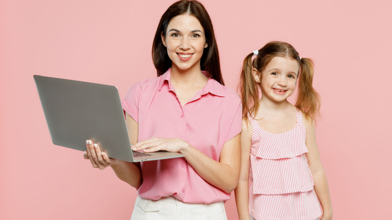 Mulher feliz, sorrindo, usando roupas casuais, ao lado de uma criança, segurando um laptop. Isoladas em um fundo rosa pastel liso.