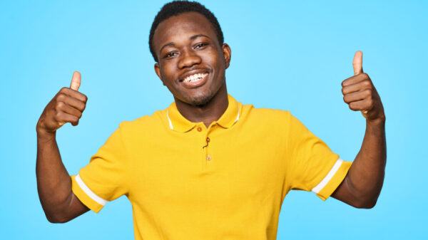 Homem alegre, usando uma camiseta amarela, em um fundo azul.