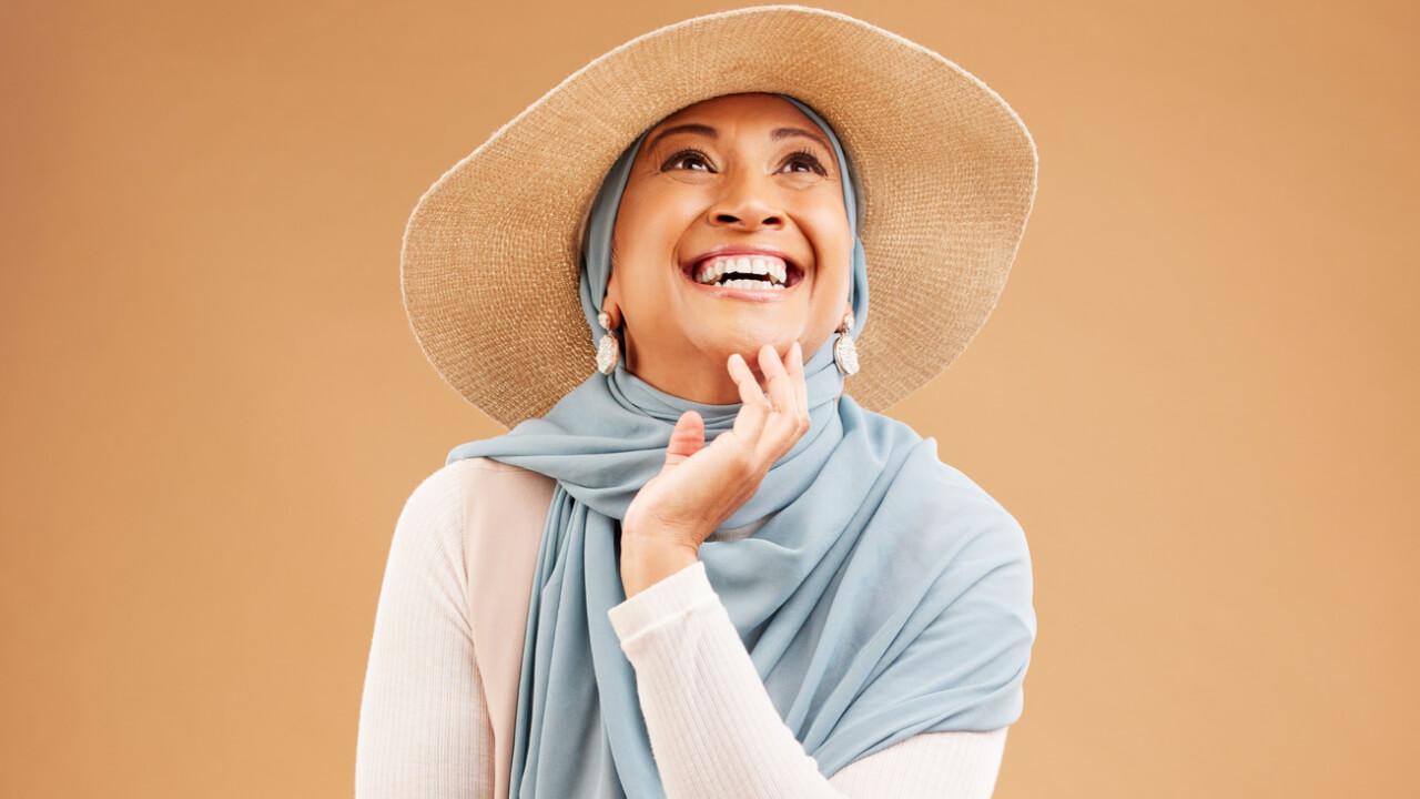 Mulher feliz, pensando, em um fundo de um estúdio, usando um chapéu moderno, rindo, com uma mentalidade positiva.