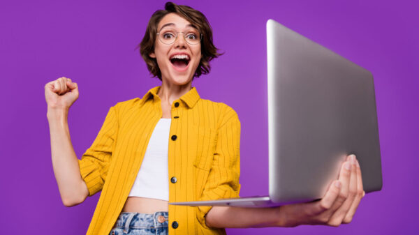 Retrato de uma mulher alegre, segurando um laptop, regozijando-se, isolada sobre um fundo de cor roxa.