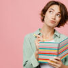 mulher pensativa com um caderno em mãos em fundo rosa