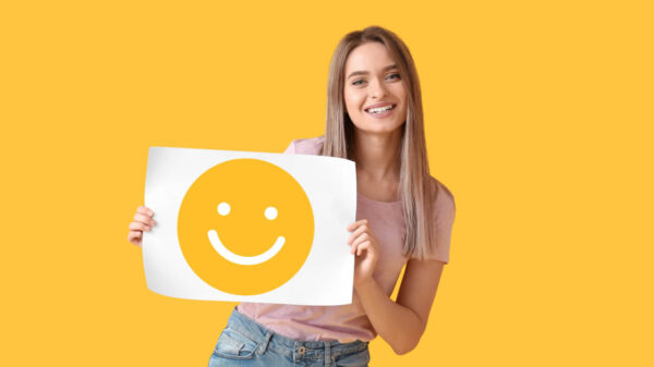 Mulher segurando um papel com um emoticon sorridente, em um fundo amarelo.