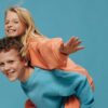 Crianças felizes e alegres, o menino levando a menina nas costas. Fotografia de estúdio em um fundo azul.