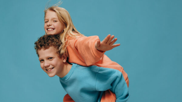 Crianças felizes e alegres, o menino levando a menina nas costas. Fotografia de estúdio em um fundo azul.
