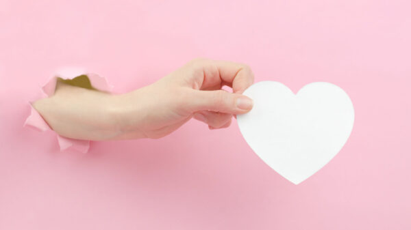 Mão segurando um papel branco cortado em um formato de coração.