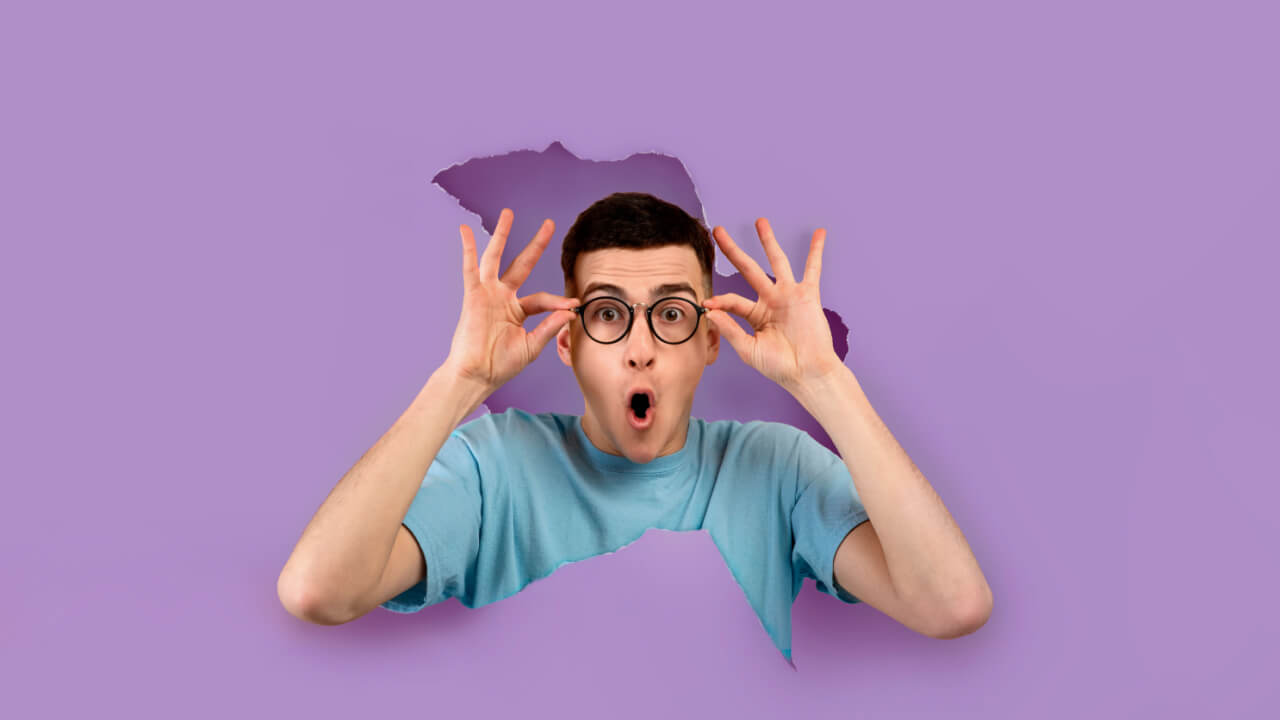 Retrato de um homem chocado, usando e segurando um óculos, com uma expressão espantada, através de um buraco rasgado de um papel violeta.