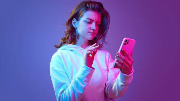 Mulher usando celular, lendo algo, contra um fundo de estúdio roxo e rosa em luz neon.