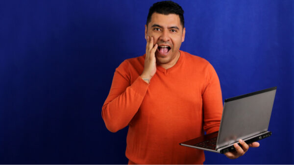 Homem de cabelos escuros, segurando um laptop, entusiasmado e com vitalidade.
