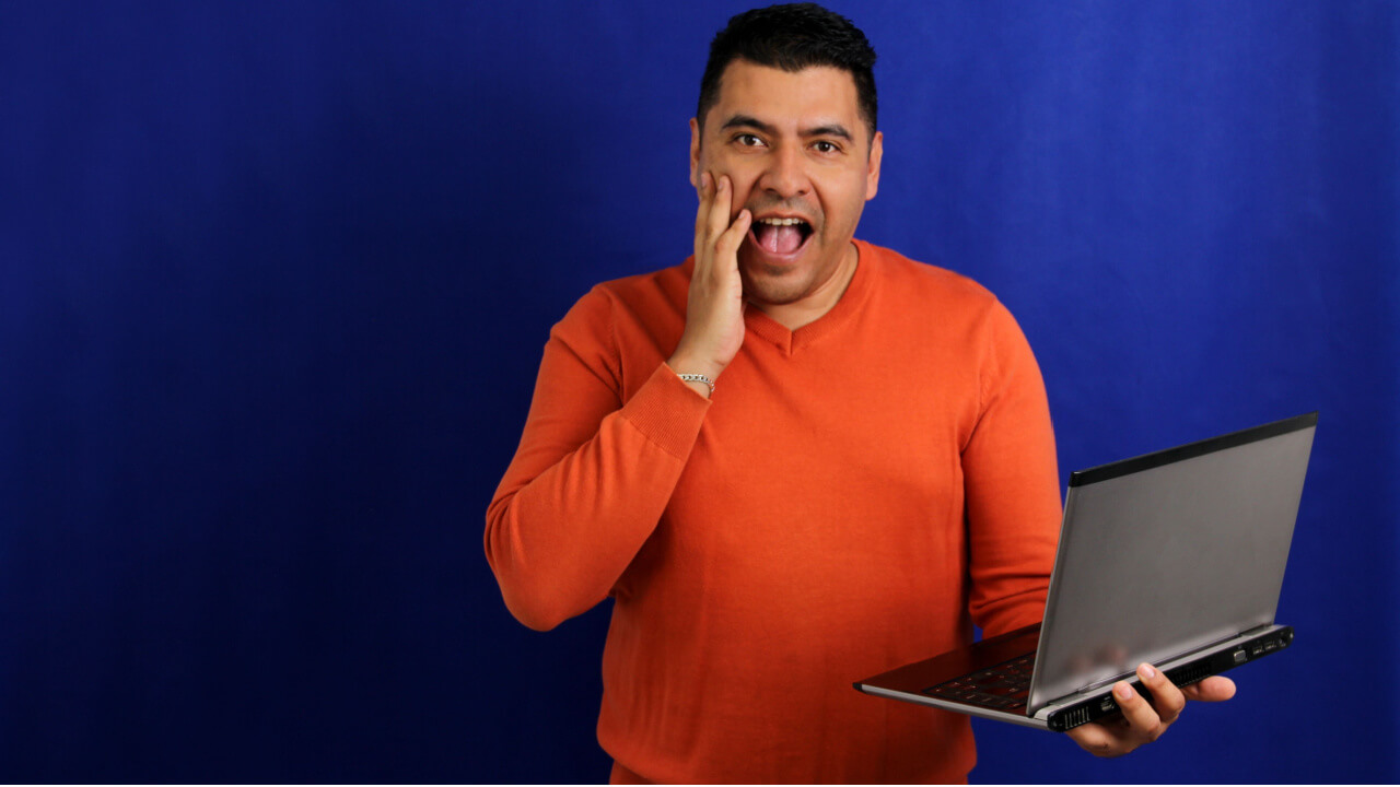 Homem de cabelos escuros, segurando um laptop, entusiasmado e com vitalidade.