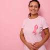 Mulher sorrindo, usando uma camiseta rosa com uma fita de cetim rosa simbolizando o Dia Internacional do Câncer de Mama, expressando solidariedade e apoio aos pacientes e sobreviventes de câncer de mama.