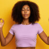mulher negra fazendo sinal de meditação com as mãos em fundo amarelo