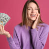 Mulher feliz, segurando notas de dinheiro, em um fundo rosa.