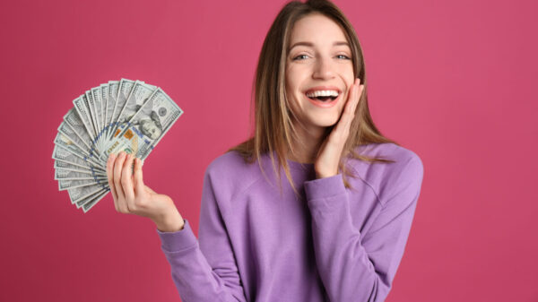 Mulher feliz, segurando notas de dinheiro, em um fundo rosa.