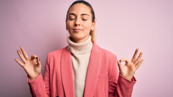 Mulher vestindo um casaco rosa, relaxando, com os olhos fechados, fazendo gesto de meditação com os dedos. Conceito de ioga e respiração.