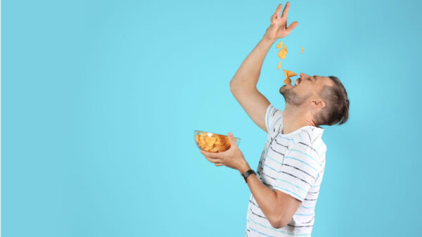 Homem comendo batatas chips em um fundo de cor azul.