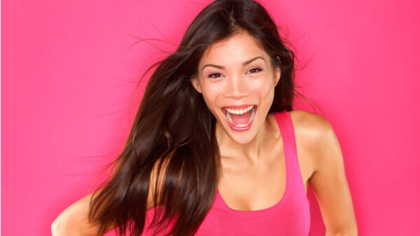 Mulher animada, alegre e sorrindo, feliz, usando um vestido rosa, em um fundo rosa.