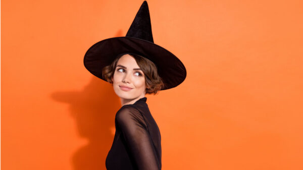 Foto de uma mulher vestida de bruxa, olhando para trás, em um fundo de cor laranja isolado.