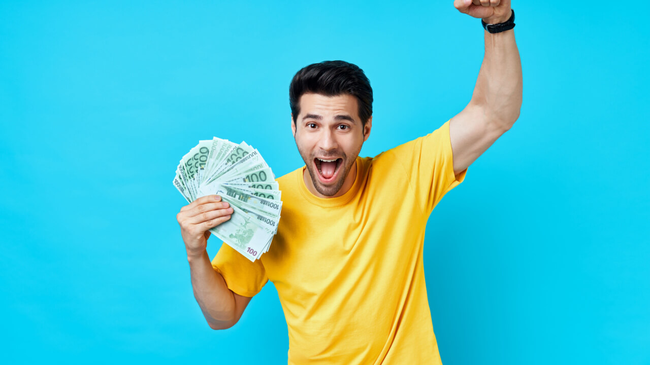 homem vestindo amarelo com um leque de dinheiro na mão esquerda em fundo azul