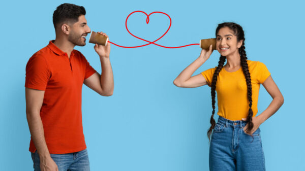 À esquerda está um homem e a direita uma mulher e os dois estão segurando um copo em que sai uma linha vermelha formando um coração em fundo azul