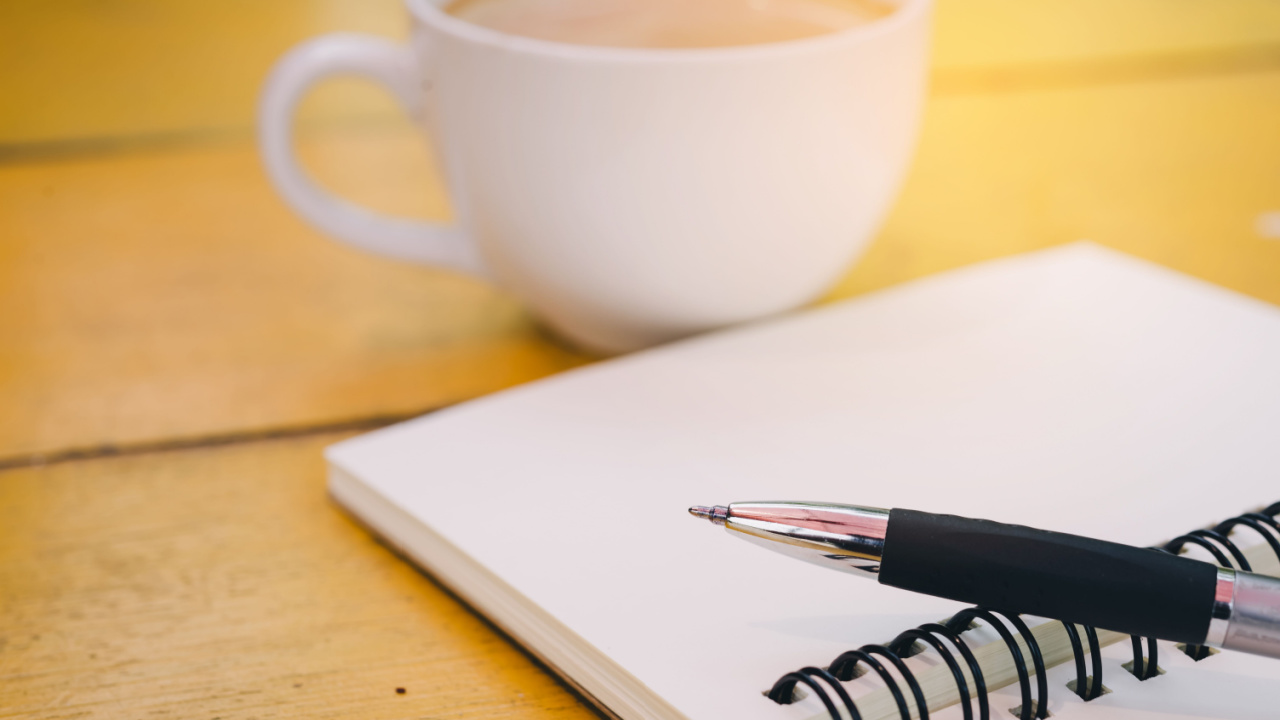 caderno, caneta e xícara branca de café em cima de uma mesa de madeira