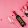 Vista superior uma garrafa de vinho com o número "2024", e um buquê de rosas, em um fundo rosa.