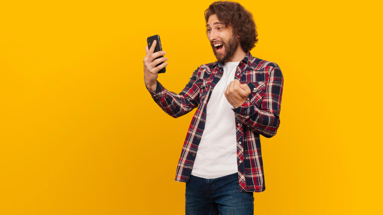 Homem, feliz, alegre, olhando para o celular em um fundo amarelo.