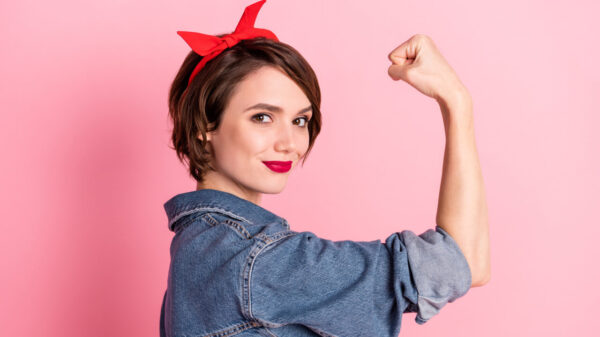 Foto de uma mulher autoconfiante, mostrando o braço fazendo o símbolo de força, isolada em um fundo de cor rosa.