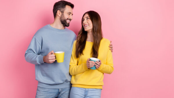 casal se abraçando e cada um segurando uma caneca em fundo rosa