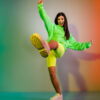 Foto de corpo inteiro de uma mulher alegre, dançando, de bom humor, isolada sobre um fundo de luz neon vívido multicolor.