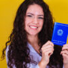 mulher sorrindo segurando uma carteira de trabalho em fundo amarelo